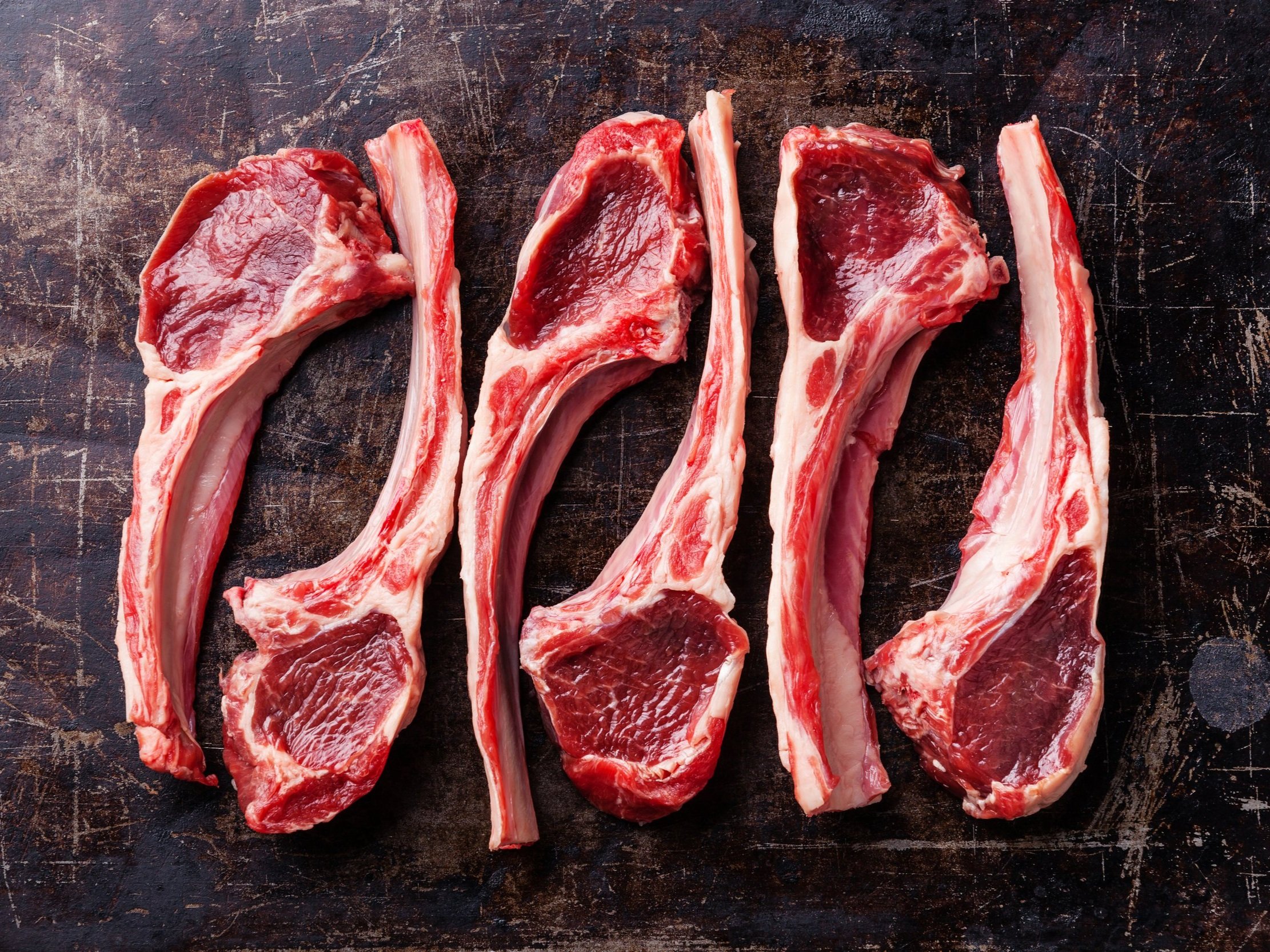 lamb_chops_raw Raw lamb chops arranged on a rustic wooden cutting board, showcasing their marbled texture and vibrant red color, ideal for grilling or roasting.