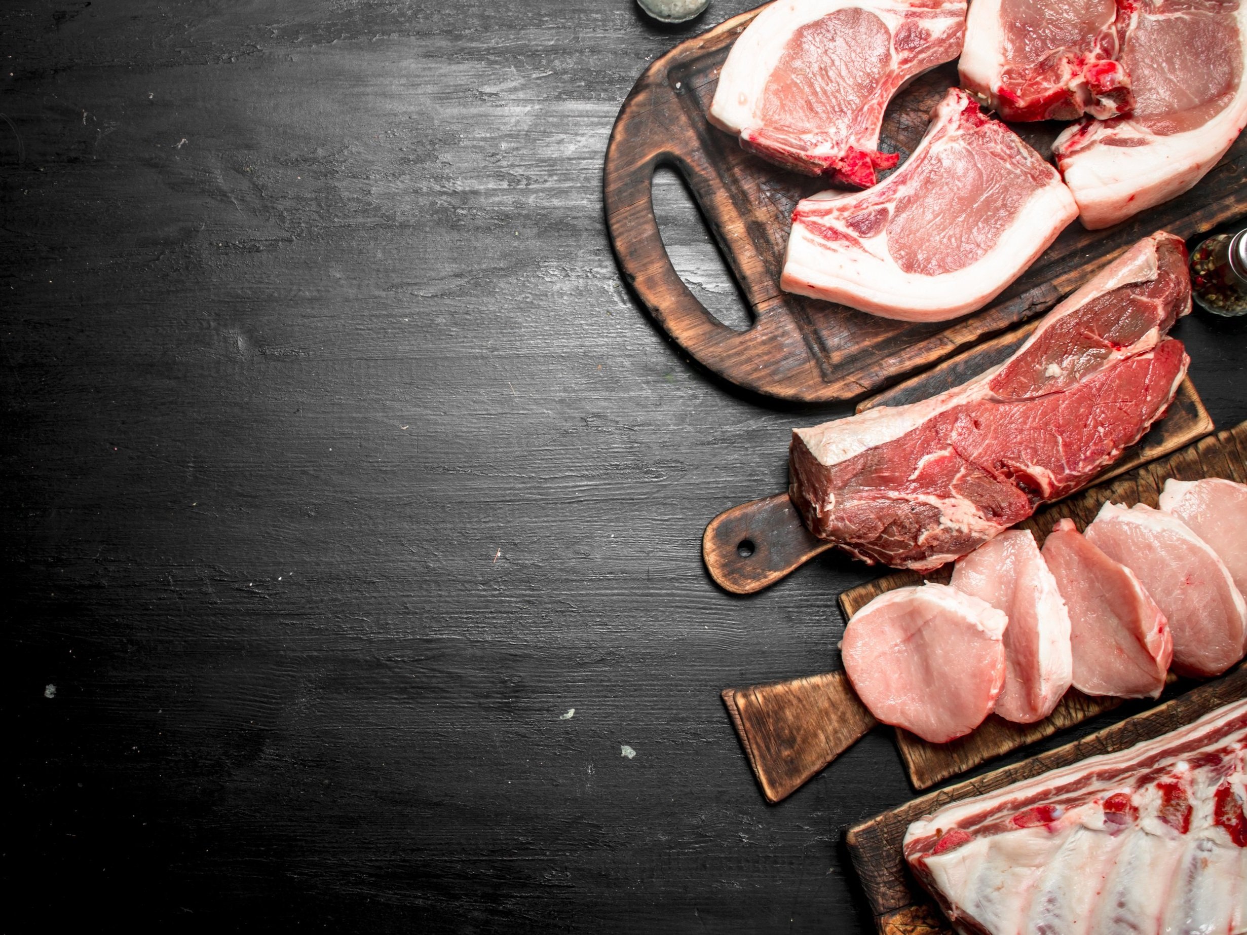 pork_cuts_mixed_rightside Assorted cuts of fresh meat displayed on wooden cutting boards, including pork chops, beef steaks, and pork loin, set against a dark background, ideal for culinary presentations or butchery showcases.
